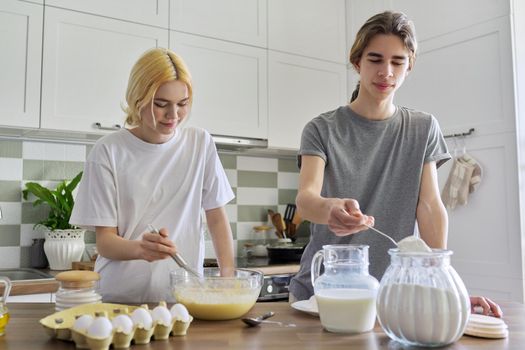 Teenagers guy and girl cooking pancakes in kitchen together. Young people, couple of friends, learning to cook, laughing, talking. Hobbies, teens, emotions, lifestyle, cooking concept