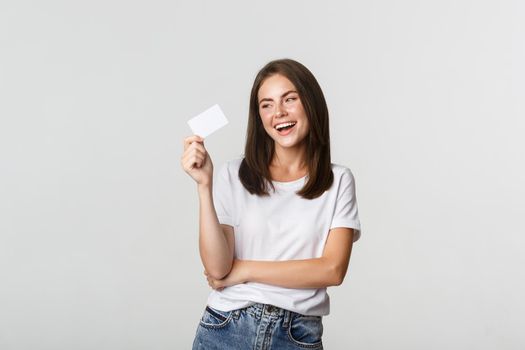 Attractive happy brunette girl laughing and holding credit card, white background.