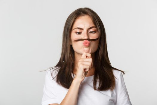 Close-up of funny cute brunette girl pouting and holding hair strand over lip playfully.