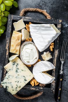 Assorted Cheese platter with Brie, Camembert, Roquefort, parmesan, blue cream cheese, grape and nuts. Black background. Top view.