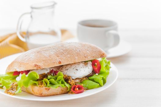 breakfast in a rustic style on a white wooden surface. ciabatta with poached egg and grain mustard with a hot cup of coffee and fresh