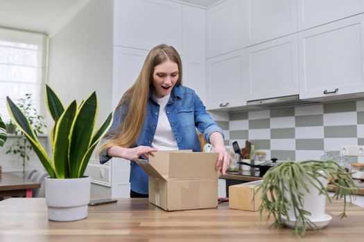 Young happy woman unpacking cardboard boxes, unboxing expected postal parcel with online shopping, at home in kitchen