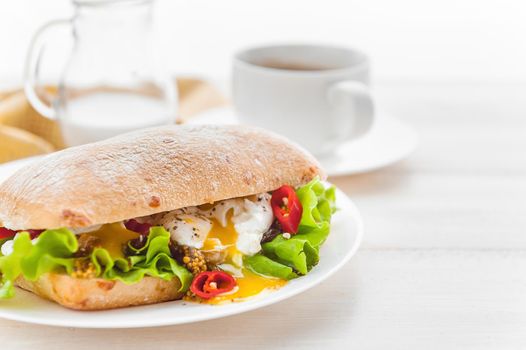 breakfast in a rustic style on a white wooden surface. ciabatta with poached egg and grain mustard with a hot cup of coffee and fresh