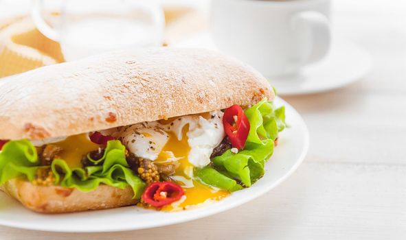 breakfast in a rustic style on a white wooden surface. ciabatta with poached egg and grain mustard with a hot cup of coffee and fresh