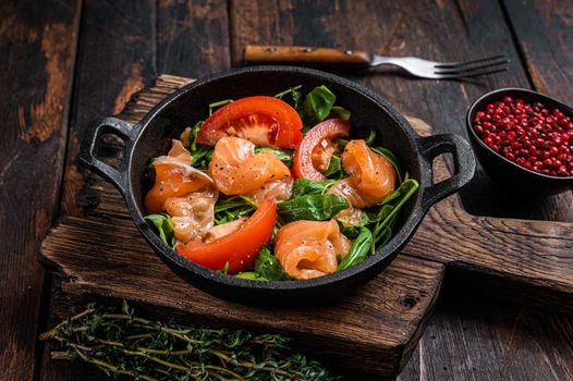 Fresh salmon salad with arugula, tomato and green vegetables. Dark wooden background. Top View.