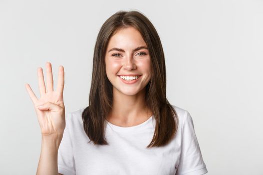 Close-up of cheerful attractive young woman smiling, showing four fingers, white background.