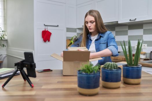 Woman recording video on smartphone moment of unpacking cardboard box. Showing purchases ordered on Internet, product quality reviews with followers, blog content, feedback. Pet parrot helping unpack