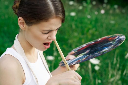 Woman in white dress with palette of paints on nature art drawing. High quality photo