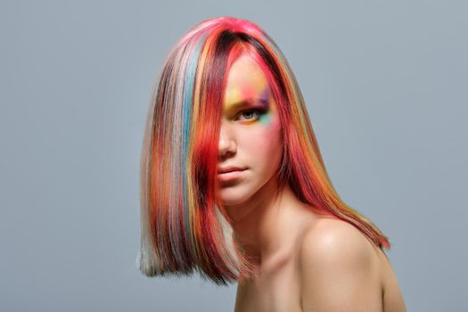 Beauty portrait, head and shoulders of a young model with colored hair and creative make-up. Close-up face and trending hairstyle, on gray studio background