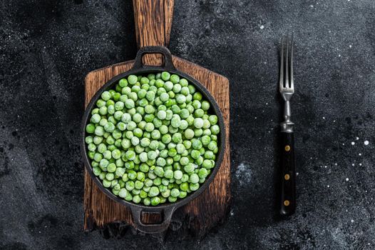 Fresh Frozen green peas in a pan. Black background. Top view.