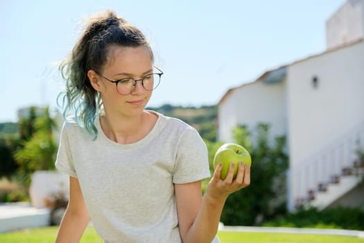 Girl teenager with green apple, female holding tasty healthy apple in hand, sunny summer day background