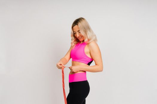 Fitness woman with tape measure showing her waist on a studio background