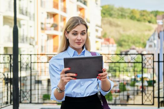 Surprised young business woman looking emotionally into digital tablet screen, on city street