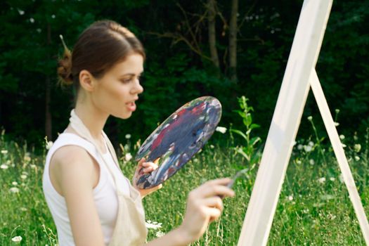 woman artist outdoors with palette of paints paints a picture. High quality photo