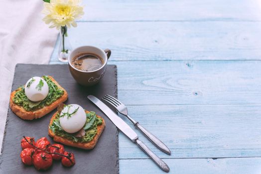 Breakfast with egg poached on avocado paddle and basil and a cup of coffee