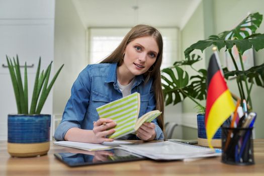 Female student looking talking to webcam, headshot portrait of young woman studying online, studying German, flag of Germany on table. E-education, e-learning, distance learning