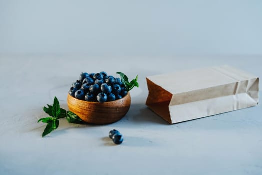 Wooden bowl with fresh blueberries and mint. A kraft bag for berries lies nearby.