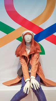 one woman mannequin in luxurious winter or autumn clothes in a shop window. A red-haired female mannequin demonstrates a casual collection of clothing. Brown coat