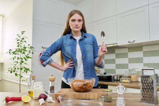 Young woman prepares chicken at home, marinates meat with spices in glass bowl on table, kitchen interior background, cook at home