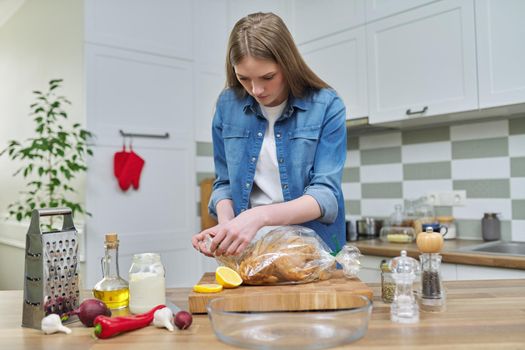 Young woman cooking baked chicken in baking sleeve with spices, kitchen interior background, cooking at home concept