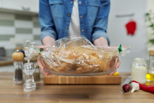 Cooking at home, close-up of marinated chicken in bakery cooking bag for roasting and hands of woman