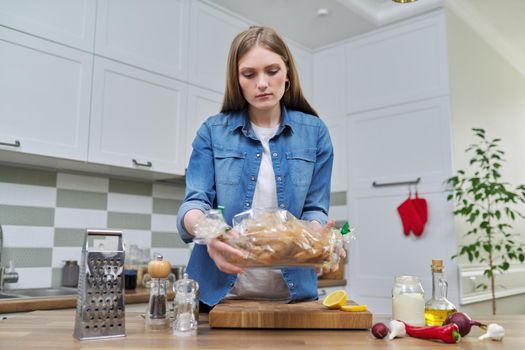 Young woman cooking baked chicken in baking sleeve with spices, kitchen interior background, cooking at home concept