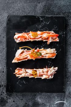 Crab leg meat in a sheel with herbs. Black background. Top view.