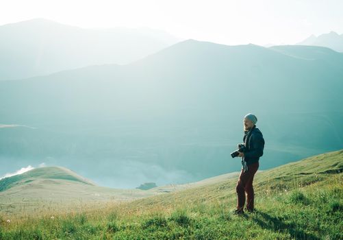 Photographer young man with photo camera walking in summer mountains.