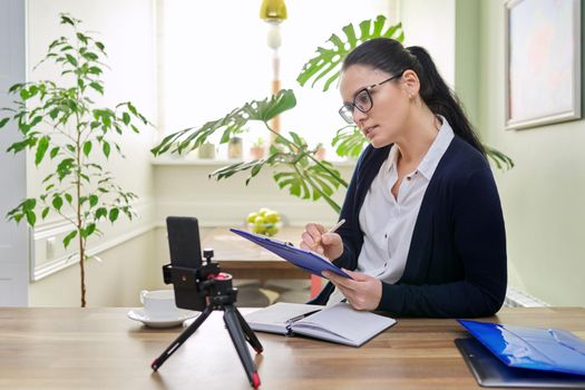 Business woman working remotely using video call. Female freelancer, teacher, psychologist, financial legal specialist sitting at home looking at smartphone webcam, talking, consulting teaching online