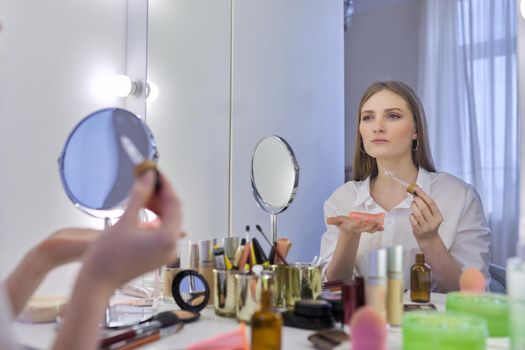 Young beautiful woman doing facial massage with silicone tools cosmetic vacuum jars, using massage oil. Female sitting at home at make-up table with mirror, caring for skin of face, home spa treatment