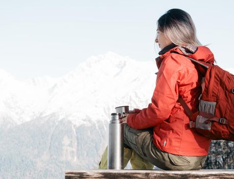 Traveler woman with backpack drinking tea in winter mountains.