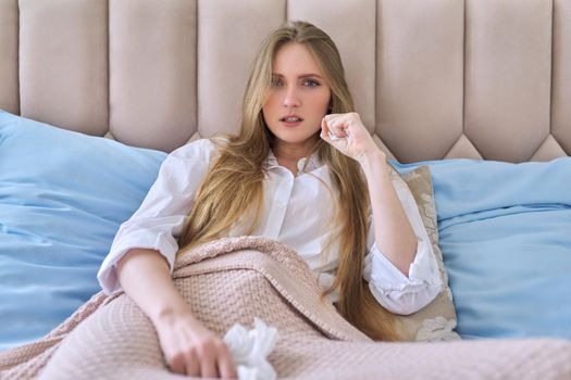 Sad unhappy crying young woman with handkerchief sitting alone at home in bed. Problems, lifestyle, youth, mental health concept