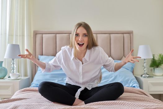 Positive beautiful young woman laughing charming smile with teeth. Lovely blonde with long natural hair sitting in lotus position in pastel pink bed