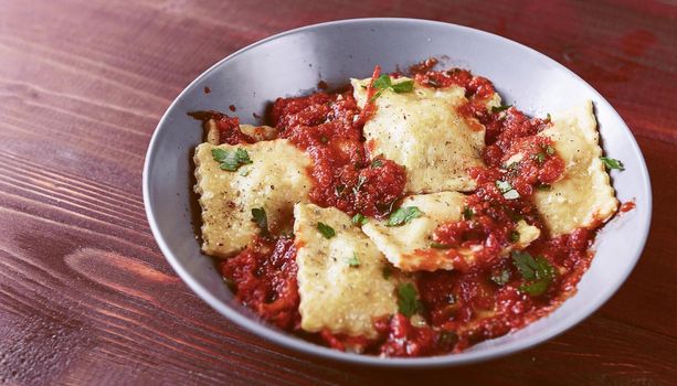 Delicious ravioli with tomato sauce in a plate on a wooden background