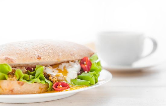 breakfast in a rustic style on a white wooden surface. ciabatta with poached egg and grain mustard with a hot cup of coffee and fresh