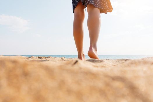 Young woman walking on sand beach, view of legs.