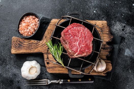 Raw fillet mignon beef steak on a grill with herbs. Black background. Top view.