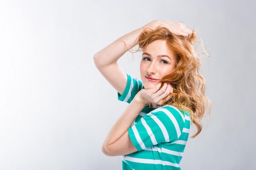 Close-up portrait of a young, beautiful woman with red curly hair in a summer dress with strips of blue in the studio on a gray background. Theme of summer vacation, tourism and summer clothes.