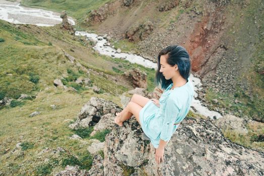 Beautiful young woman sitting on cliff over mountain river.