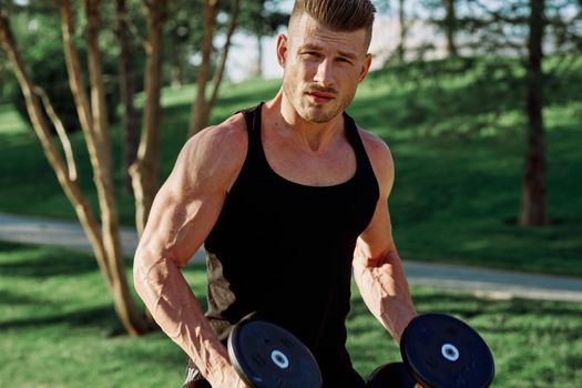 athletic man in black t-shirt with dumbbells in the park training. High quality photo