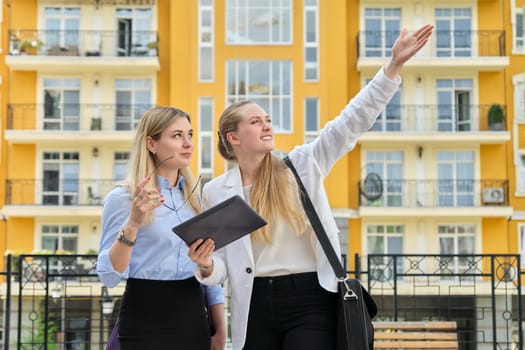 Two young businesswomen on city street, talking and looking in screen of digital tablet. Business, people, technology, teamwork, communication, lifestyle concept