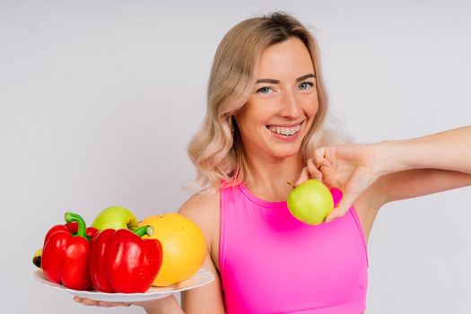 Studio shot of young fitness woman in a sports clothing holding green apple, fruits, vegetables.