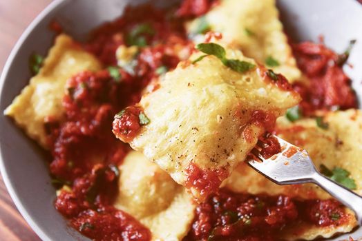 Delicious ravioli with tomato sauce in a plate on a wooden background