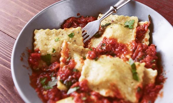 Delicious ravioli with tomato sauce in a plate on a wooden background