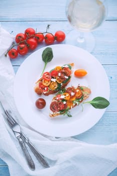 Bruschetta with cheese, basil, arugula and cherry tomatoes and a glass of white wine