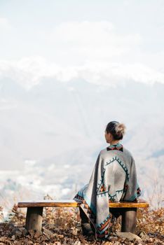 Young woman resting on a bench on viewing platform in front of mountains.