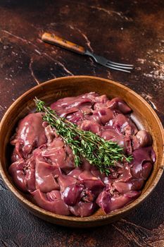 Raw chicken liver offals in a wooden plate. Dark background. Top view.