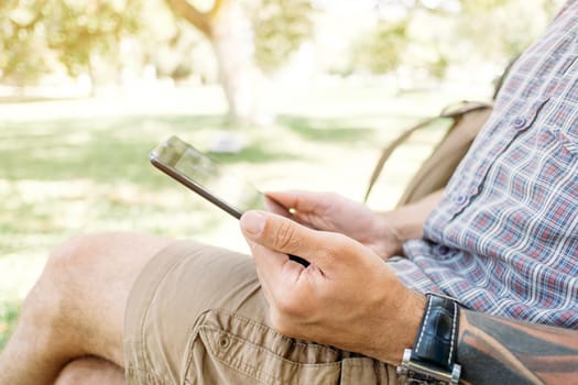 Unrecognizable young man sitting in park with digital tablet.