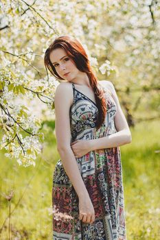 Portrait of carefree young woman in boho style dress in spring cherry blossom garden.