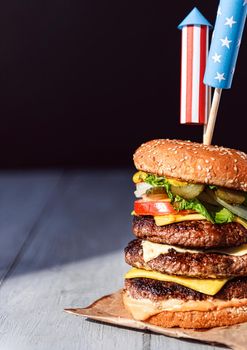 a big burger with three juicy beef patties bonded with American flag firework skewers. burgar concept for the day of independence day celebration of fourth of july